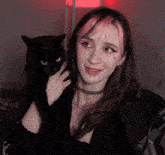 a woman with pink hair holds a black cat in her arms