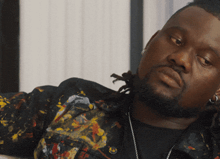 a man with dreadlocks is wearing a colorful jacket and black shirt
