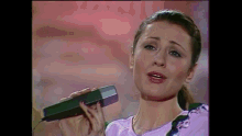 a woman in a purple shirt is singing into a microphone .