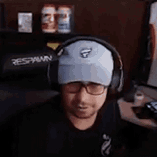 a man wearing headphones and a hat is smiling while sitting at a desk .