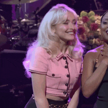 a woman in a pink crop top smiles while standing next to a woman in a black dress