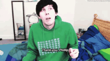 a man in a green hoodie is sitting on a bed and saying `` thank you , phillip '' .