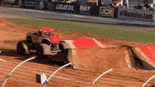 a monster truck is driving down a dirt track in front of a lucas oil banner