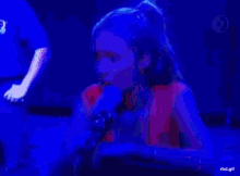 a woman in a red shirt is singing into a microphone with rbd.gif below her