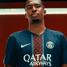 a man wearing a qatar airways jersey stands in front of a red wall