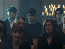 a group of people sitting in a dark room with candles hanging from the ceiling