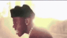 a man wearing a hat and a pearl necklace is standing in front of a yellow background .