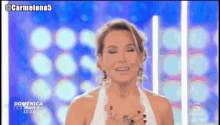 a woman in a white dress is smiling in front of a screen that says domenica 17:23