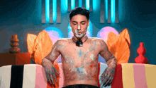 a shirtless man with a necklace on his neck is covered in paint