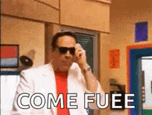 a man wearing sunglasses and a white suit is talking on a cell phone and the words come fuee are visible .