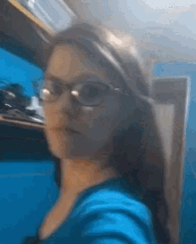 a woman wearing glasses and a blue shirt is taking a selfie .