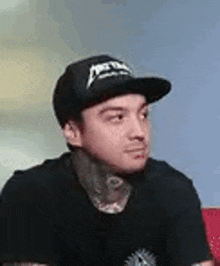 a man wearing a hat and a black t-shirt is sitting on a couch .