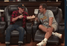 a man wearing a shirt that says monsters sits next to another man in a chair
