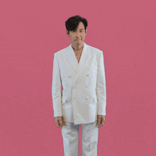 a man in a white suit with his arms outstretched on a pink background