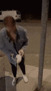a woman is standing on a sidewalk next to a pole holding a white cat .