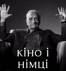 a man in a suit sits in a chair with his hands in the air and the words kino i himchi on the bottom