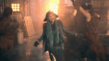 a woman with blue dreadlocks and a pirate hat is laughing in front of a fire