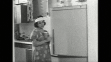 a black and white photo of a woman opening a refrigerator door
