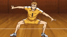 a man in a yellow shirt and shorts is squatting on a volleyball court with his arms outstretched .