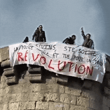 a group of people standing on top of a building holding a banner that says revolution