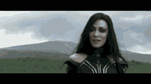 a woman in a superhero costume is standing in a field with mountains in the background .