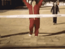 a man in a red jumpsuit is jumping over a white line .
