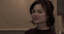 a woman is smiling and looking at the camera while wearing a maroon sweater .