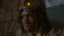 a man with dreadlocks wearing goggles and a plaid jacket looks at the camera