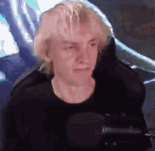 a man with blonde hair is sitting in front of a microphone and making a funny face
