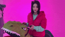 a woman in a red jacket is standing in front of a pink wall holding a cane .
