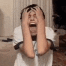a young boy is holding his head with his hands while screaming .