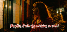 a woman in a red jacket is standing in front of a building with the words " en plus il y a hyper bien ce con "