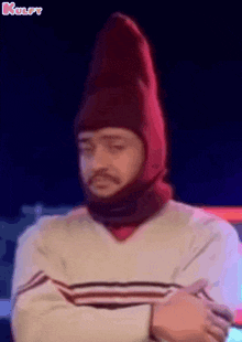 a man wearing a red hat and scarf is standing with his arms crossed