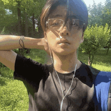 a young man wearing glasses and ear buds is standing in a park