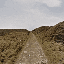 a dirt road going up a hill with a fence on the side