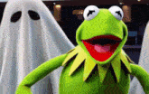 kermit the frog is standing in front of a ghost .