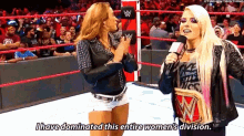 two women are talking in a wrestling ring and one of them is holding a wrestling championship .