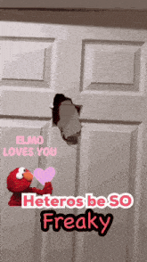 elmo is holding a heart in front of a door that says heteros beso freaky