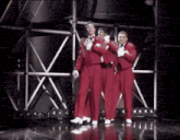 three men in red tuxedos and white gloves are dancing on a stage