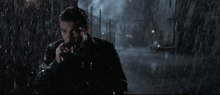 a man smoking a cigarette in the rain with a car in the background