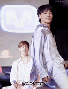 a man in a blue shirt says " feelin ' himself " in front of another man