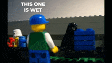 a lego man in a blue hard hat stands in front of a brick wall with the words " this one is wet " written above him