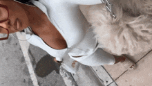 a woman in a white jumpsuit is standing next to a white dog on a sidewalk .