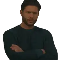 a man with his arms crossed and a beard is wearing a blue shirt