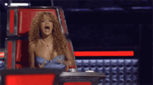 a woman is sitting in a red chair with her mouth open