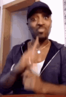 a man wearing a hat and a necklace is making a gesture with his hands .