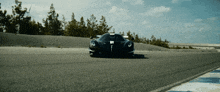 a black sports car is driving down a track with a few trees in the background