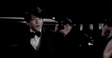 a man in a tuxedo and bow tie is standing in front of a car at night .