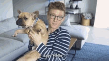 a man in a striped shirt is holding a dog and says " say hello "