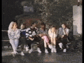 a group of people are sitting on a bench and talking to each other .